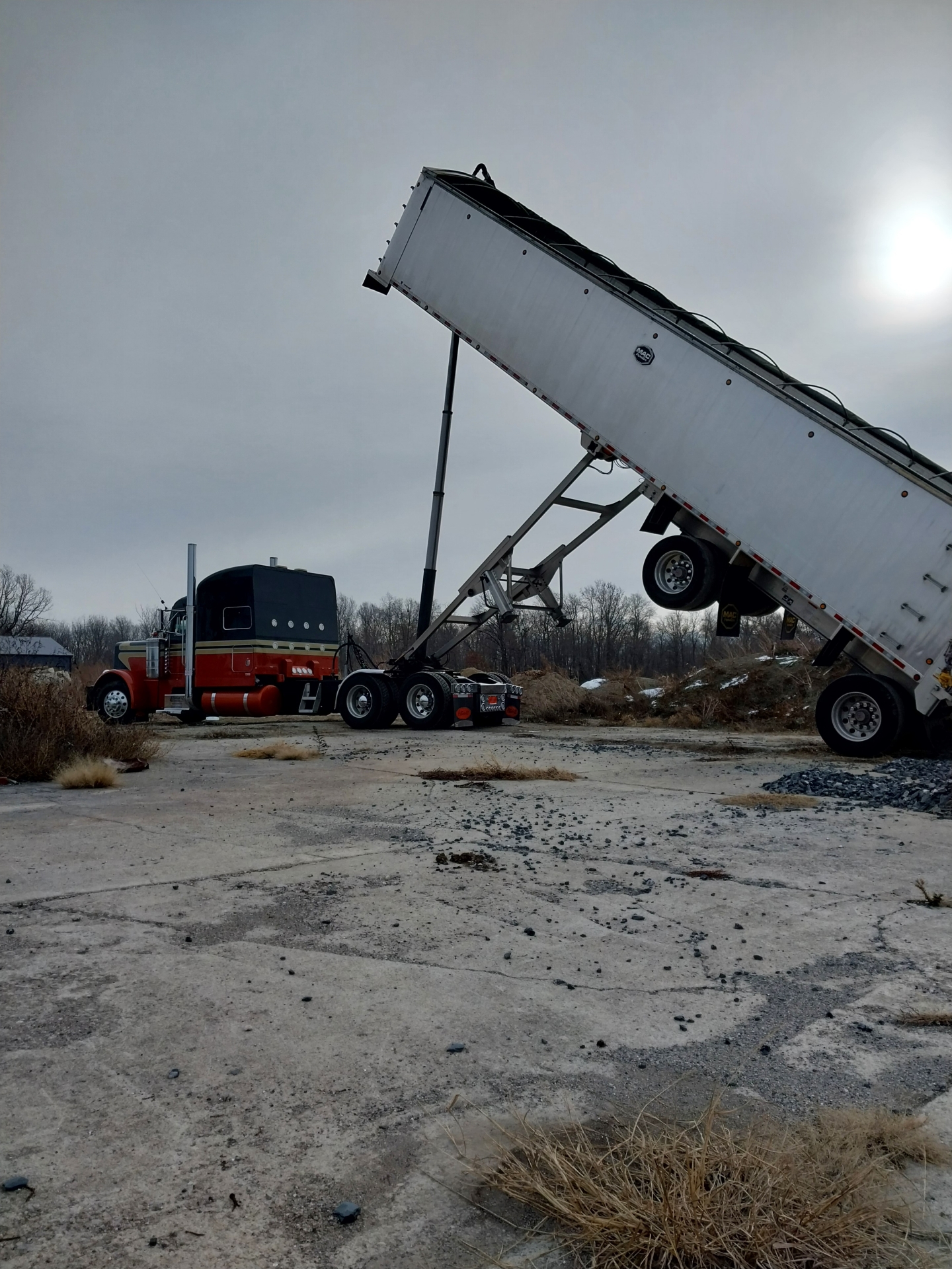 Semi-truck with tipped trailer unloading in field.