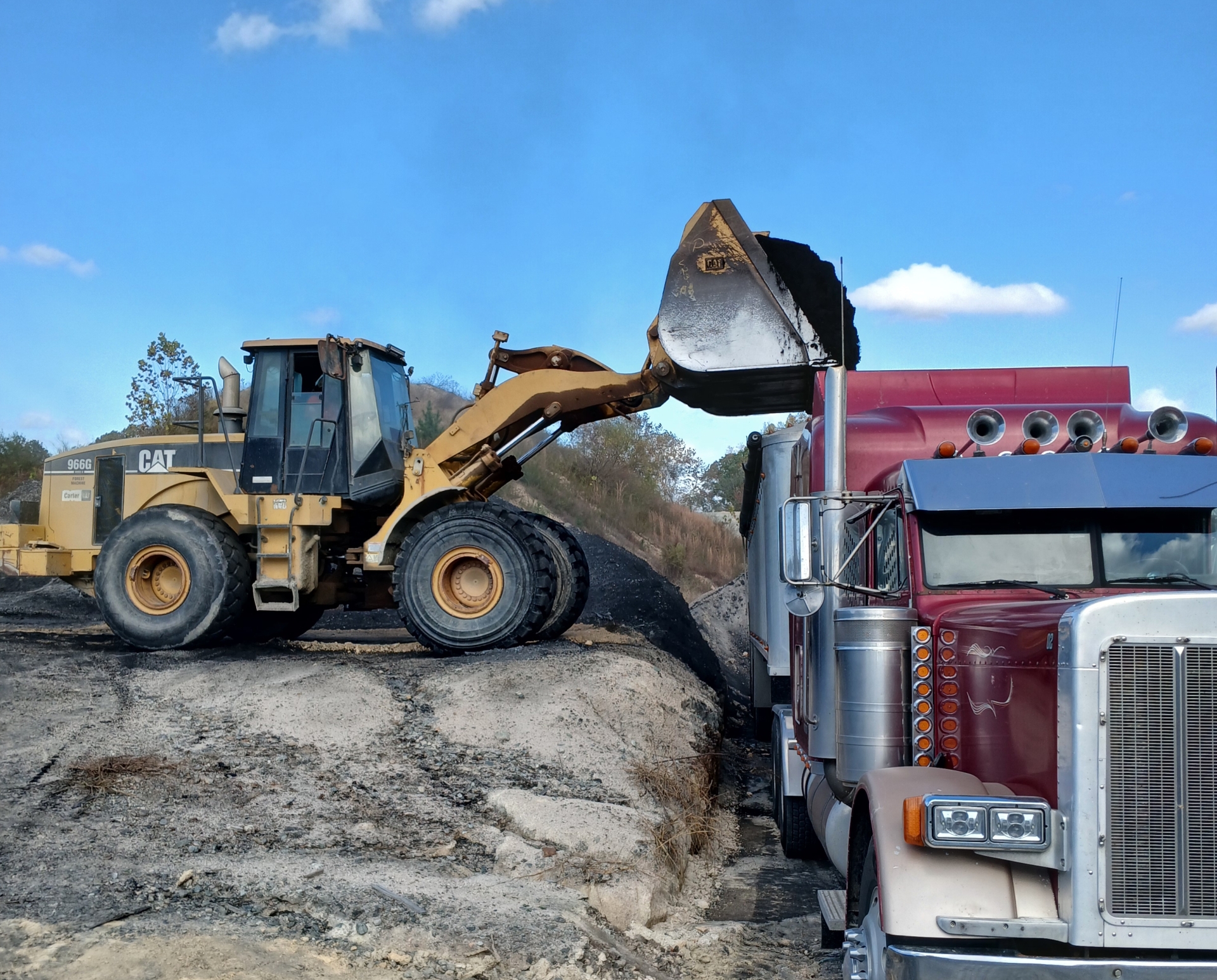 Front loader loading truck with soil at construction site.