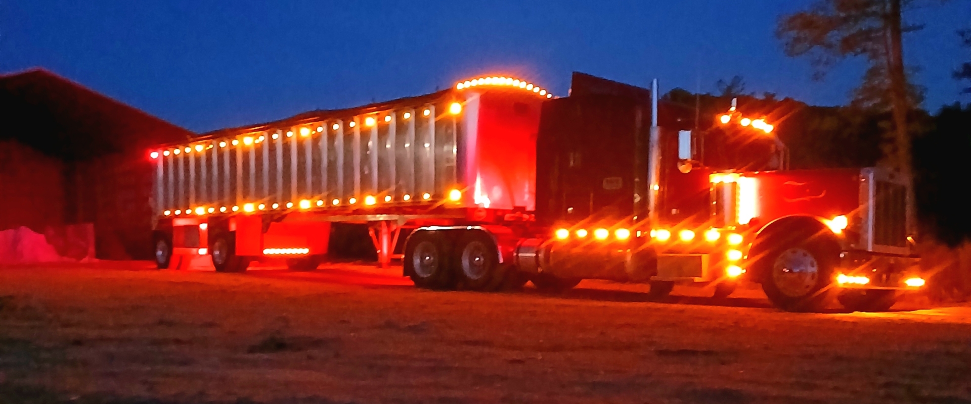 Illuminated semi-truck parked at night near barn.