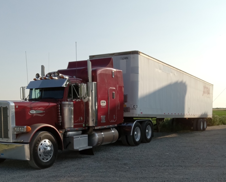 Red semi-truck hauling large white trailer parked.